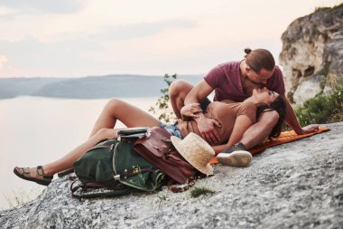 Sırt çantalı çift kaya dağının tepesinde oturmuş nehir ya da göl manzarasının keyfini çıkarıyorlar. Dağları ve kıyıları dolaşmak, özgürlük ve aktif yaşam tarzı kavramı.