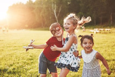 Erkek ve iki kız kardeş birlikte oynuyorlar. Üç çocuk dışarıda tahta bir uçakla oynuyor..