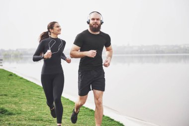 Couple jogging and running outdoors in park near the water. Young bearded man and woman exercising together in morning.