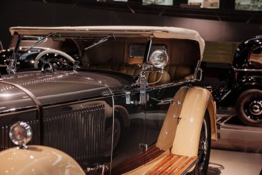 Araba fuarı. Arka planda bir otomobil daha. Yan tarafında farlar olan gümüş sarısı renkli aracın ön tarafı..