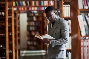 An African American man in a business suit standing in a library in the reading room clipart