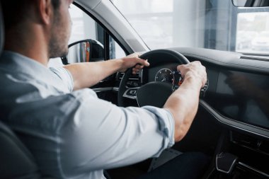 Genç bir adam yeni alınmış bir arabada oturuyor ve ellerini dümene koyuyor.