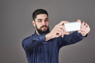 Yenilikçi iş adamı selfie fotoğraf gülümseyen ve telefon gri studio arka plan bakarak akıllı telefon ile konuşurken Genç sakallı.