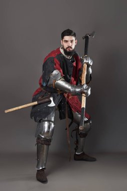 Gri arka planda ortaçağ şövalyesi. Zincirli zırhlı, kırmızı, siyah elbiseli ve savaş baltalı zalim, kirli yüzlü bir savaşçı portresi..