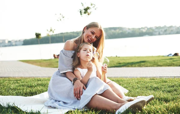 誇り高いお母さんは娘を見ている 若い母親と彼女の娘の写真バックグラウンドで湖と緑の芝生の上で楽しい時間を過ごして — ストック写真