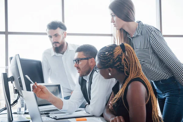 Genç çalışanlar masadaki ofiste oturuyor ve bir dizüstü bilgisayar kullanıyorlar, bir ekip beyin fırtınası konsepti üzerinde çalışıyor.