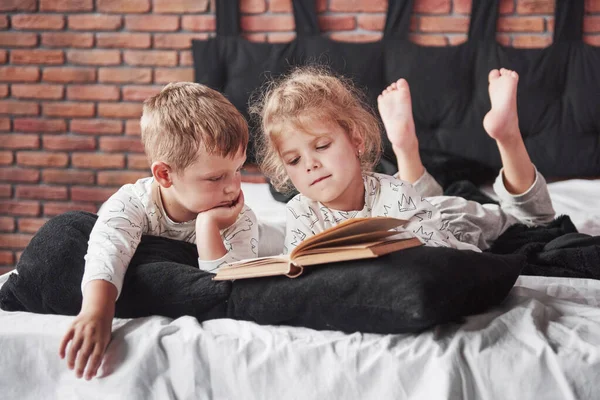 Двое Детей Лежат Большой Кровати Читают Интересную Книгу Одеты Одну — стоковое фото