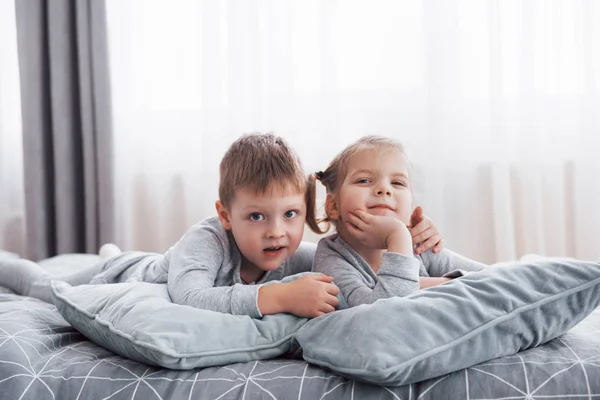 白い寝室で遊んで幸せな子供たち 男の子と女の子 弟と妹は パジャマを着てベッドの上プレイします 子供の保育園のインテリア ナイトウェア 赤ちゃんや幼児の寝具 家庭で — ストック写真