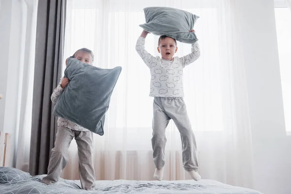 白い寝室で遊んで幸せな子供たち 男の子と女の子 弟と妹は パジャマを着てベッドの上プレイします 子供の保育園のインテリア ナイトウェア 赤ちゃんや幼児の寝具 家庭で — ストック写真