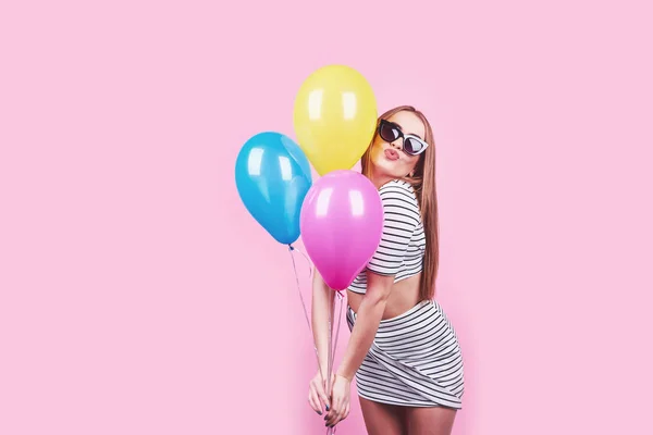 Happy smiling woman is looking on an air colorful balloons having fun over a pink background.