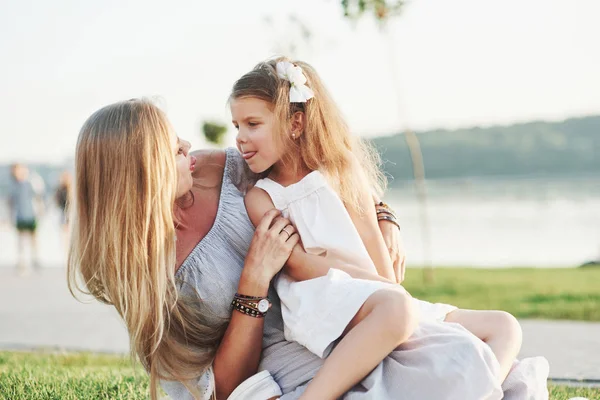 Takılıyorum Genç Anne Kızının Arka Planda Gölle Birlikte Yeşil Çimlerde — Stok fotoğraf