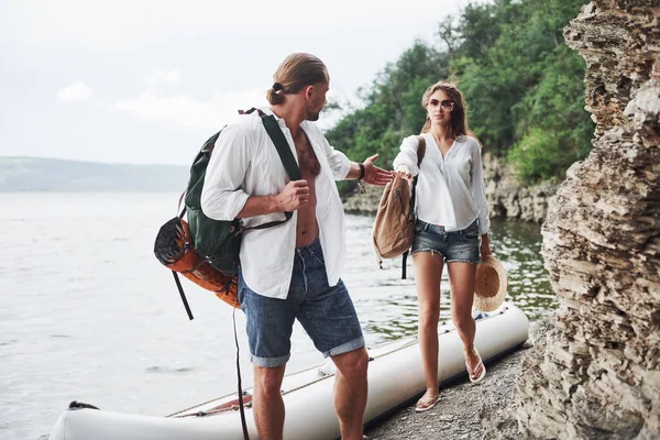 かわいい若いと川の背景にカップル バックパックを持った男と女が船で旅をしている 旅人夏のコンセプト — ストック写真