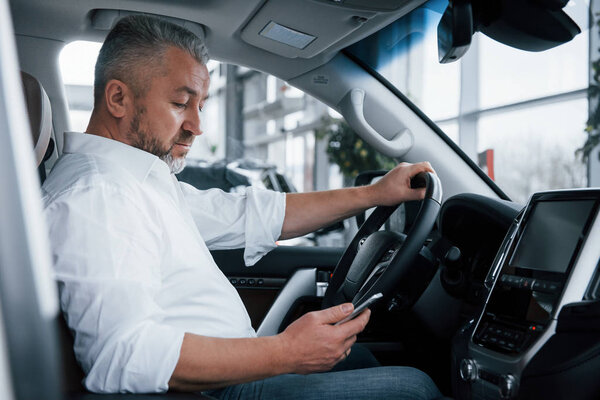 In the auto saloon. Using mobile phone. Businessman sits in the modern car and have some deals.