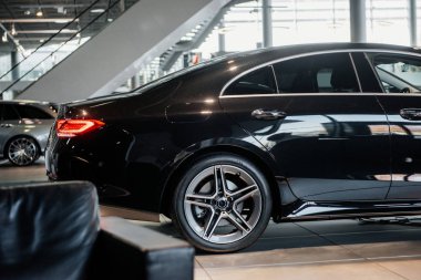 Koltuk, diğer araba ve merdivenler arka planda. Otomobil fuarında duran modern siyah arabanın yan fotoğrafı..