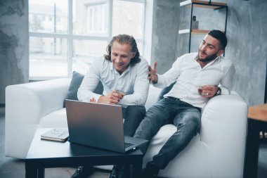 Cheerful atmosphere. Two businessman sitting in front of laptop talking about their plans.