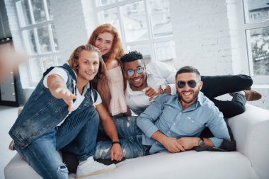 Şık kıyafetler. Arka planda pencereleri olan güzel insanlar kanepede oturuyor..