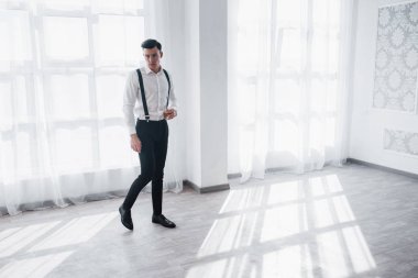 Dinlenmek ve işi düşünmek. Lüks takım elbiseli bir adam elinde viskiyle beyaz bir odada yürüyor..