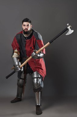 Gri arka planda ortaçağ şövalyesi. Zincirli zırhlı, kırmızı, siyah elbiseli ve savaş baltalı zalim, kirli yüzlü bir savaşçı portresi..