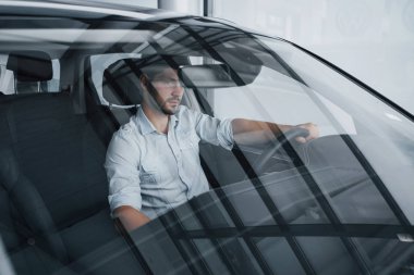 Genç bir adam yeni alınmış bir arabada oturuyor ve ellerini dümene koyuyor.