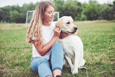 Parkta yeşil çimlerin üzerinde güzel bir köpeği olan güzel bir kızı çerçevelet.