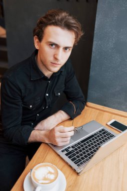 Onun en sevdiğim kafede kapalı, siparişler için beklerken kendi dizüstü bilgisayarında çalışan erkek öğrenci net-kitap üzerinde sabah kahvaltı sırasında modern kahve dükkanı iç çalışma yaratıcı adam tasarımcı.