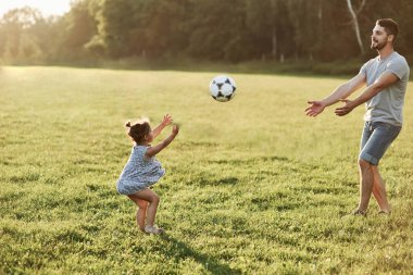 Yakalamaya çalışıyorum. Babasının kızıyla birlikte arka planda güzel çim ve ormanlara top atarken fotoğrafı..