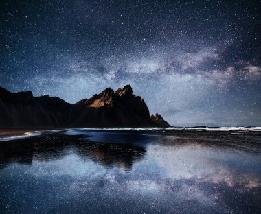 Yıldızlı gecede suya yansıyan inanılmaz dağlar. Stoksnes, İzlanda.