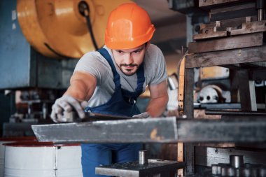 Büyük bir metal fabrikasında kasketli genç bir işçinin portresi. Makinelere hizmet eden mühendis, gaz ekipmanları için parça üretiyor..