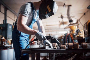 Büyük bir metal fabrikasında çalışan genç bir işçinin portresi. Kaynak mühendisi koruyucu bir maskeyle çalışıyor..