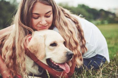 Parkta yeşil çimlerin üzerinde güzel bir köpeği olan güzel bir kızı çerçevelet.