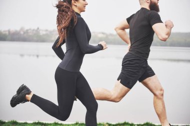 Couple jogging and running outdoors in park near the water. Young bearded man and woman exercising together in morning.