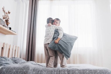 Beyaz yatak odasında oynayan mutlu çocuklar. Küçük çocuk ve kız kardeşi ve kız kardeşi pijama giymiş yatağa oynamak. Çocuklar için kreş iç. Kıyafeti ve yatak takımları bebek ve yürümeye başlayan çocuk için. Aile evde