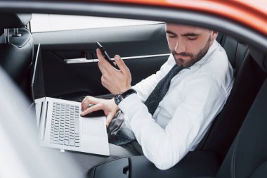 Genç bir iş adamı dizüstü bilgisayarda çalışıyor ve arabanın arkasında otururken telefonla konuşuyor. Hareket halinde çalışır, zamanını takdir eder..