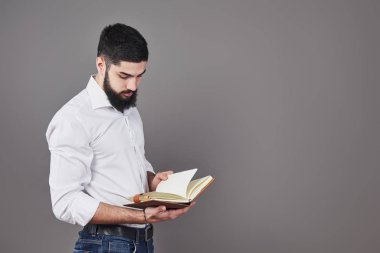 Beyaz gömlek giyen, elinde açık bir planlamacı ve kalem tutan sakallı bir gencin portresi. Gri duvar arkaplanı.