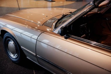 Krom pencere süslemeli, cam silecekli, aynalı, parlak kapüşonlu, direksiyonlu, sol kapılı ve açık renk lastikli bej renkli arabanın yan görüntüsü..