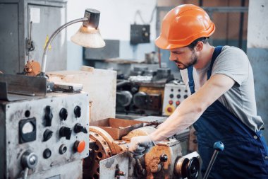 Büyük bir metal fabrikasında kasketli genç bir işçinin portresi. Makinelere hizmet eden mühendis, gaz ekipmanları için parça üretiyor..