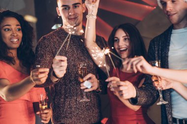 Anıların tadını çıkar. Çok ırklı arkadaşlar yeni yılı kutluyor. Bengal ışıkları ve bardaklarla içki içiyorlar..