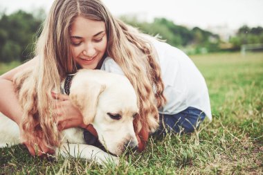 Parkta yeşil çimlerin üzerinde güzel bir köpeği olan güzel bir kızı çerçevelet.