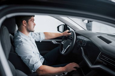 Genç bir adam yeni alınmış bir arabada oturuyor ve ellerini dümene koyuyor.