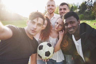 Gündelik kıyafetli bir grup arkadaş futbol sahasında sefi yapıyor. İnsanlar eğleniyor ve eğleniyor. Aktif dinlenme ve manzaralı gün batımı.