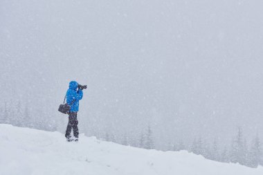 Sırt çantalı bir adam kar fırtınası üstüne kozalaklı ormanı aşıyor. Arka plan, ayarlanmış resim.