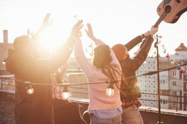 Şapkalı adam müzik aletini kaldırdı. Eller yukarı! Gençler güneşli bir sonbahar gününü çatıda gitar ve içkilerle geçirirler..