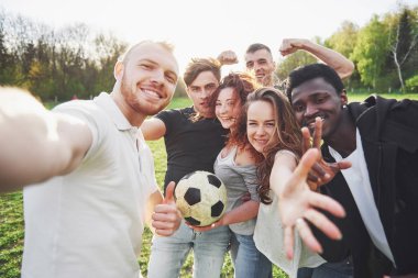 Gündelik kıyafetli bir grup arkadaş futbol sahasında sefi yapıyor. İnsanlar eğleniyor ve eğleniyor. Aktif dinlenme ve manzaralı gün batımı.