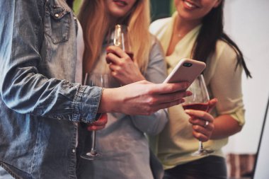 Mutlu bir arkadaş grubunu kırmızı şarapla sunan bir resim. Birlikte akıllı telefondan bir fotoğraf görüyorlar..