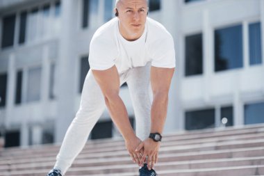 Spor kıyafetli yakışıklı bir fitness adamı, modern şehirde ciddi egzersizlere hazırlanırken esneme hareketleri yapıyor..