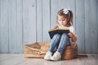 Büyük seyahate hazırız. Küçük mutlu kız büyük bir evrak çantası taşıyan ilginç bir kitap okuyor. Özgürlük ve hayal gücü kavramı.