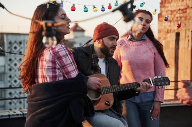 Üç arkadaş çatıda akustik gitar şarkıları söyleyerek eğleniyor..