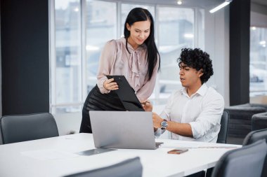 Adam belgenin anlamını açıkladı. Kıvırcık çocuk ve esmer kız modern ofiste sözleşmenin detaylarını tartışıyor..