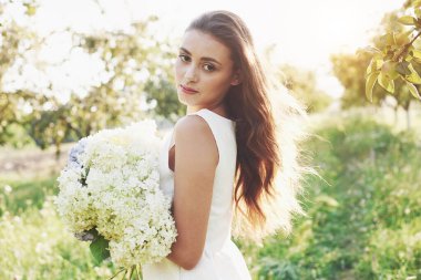 Beyaz bir elbise ve bir buket yaz çiçeği içinde güzel bir genç kız bahçede güzel bir gün geçiriyor..