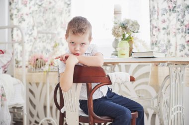 Mavi pantolonlu küçük çocuk odadaki ahşap sandalyede oturuyor. Ödev yapıyor. Okula geri dön..